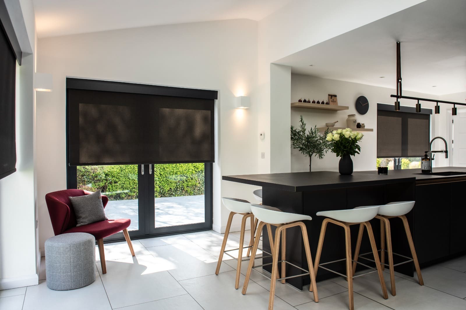 Black roller blinds in a modern kitchen with a dark island and bar stools