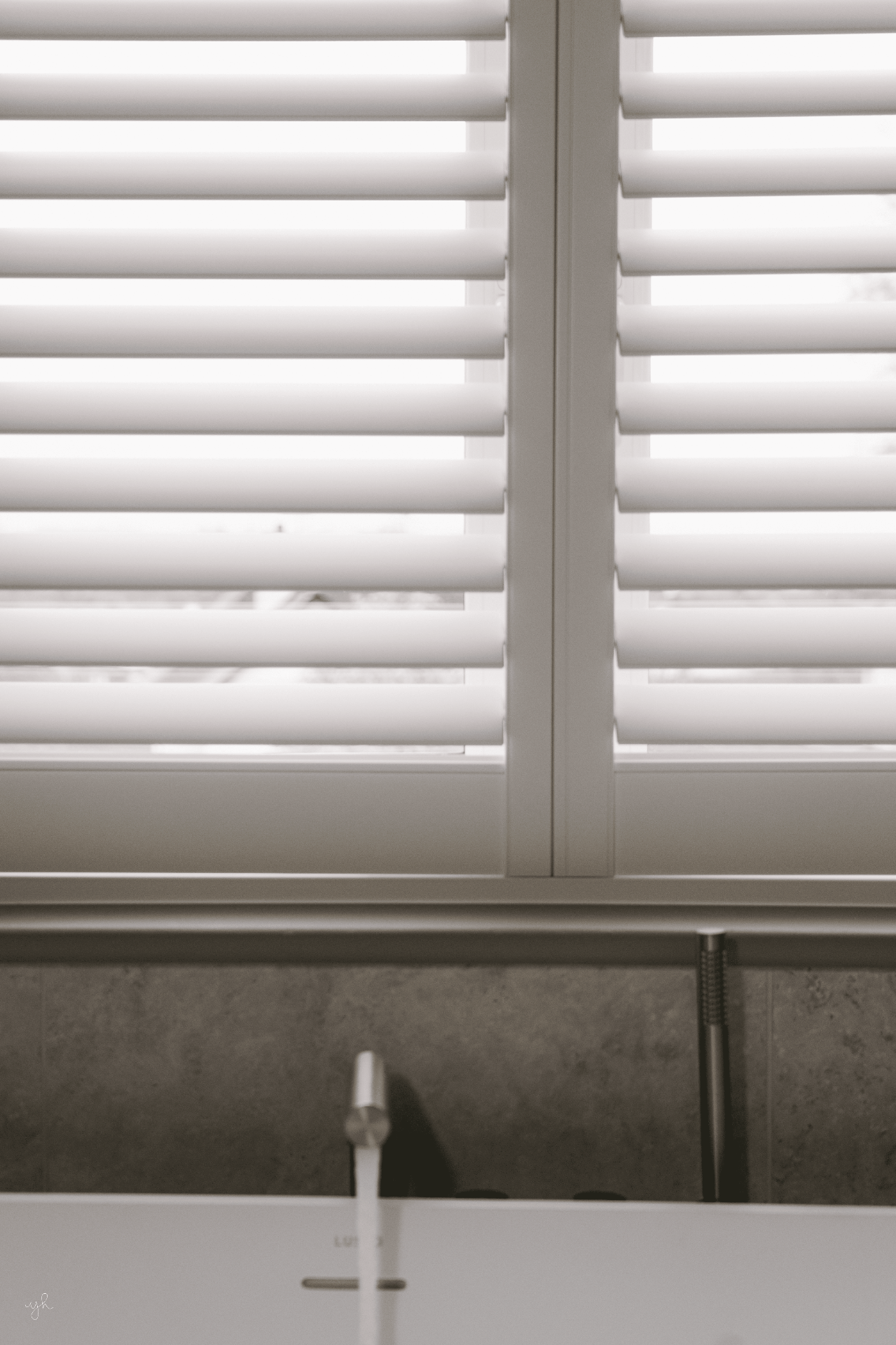 Straight-on view of white shutters above a stone bath surround with a chrome tap