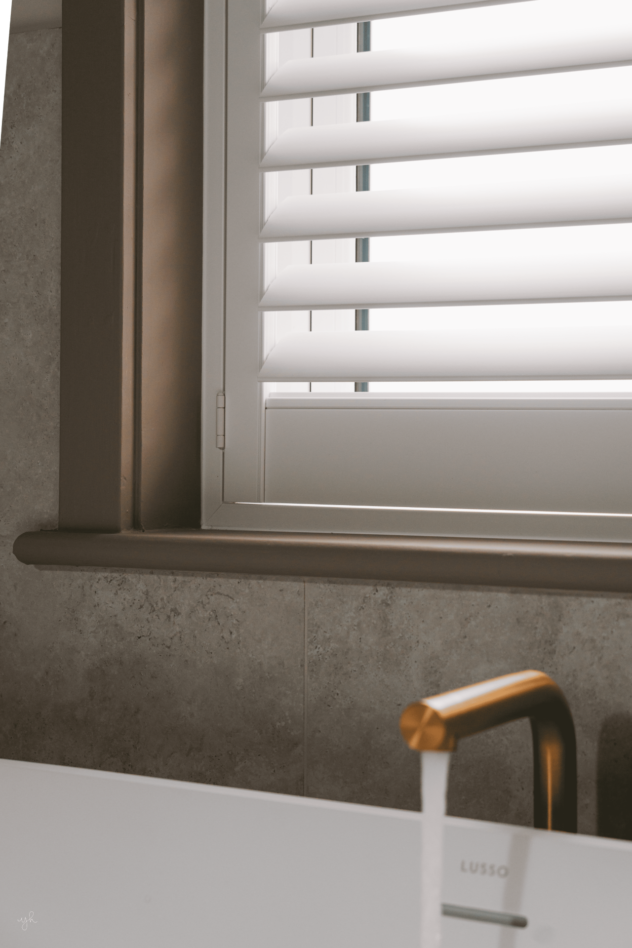 Side-angle view of white shutters above a stone bath surround with a brass tap