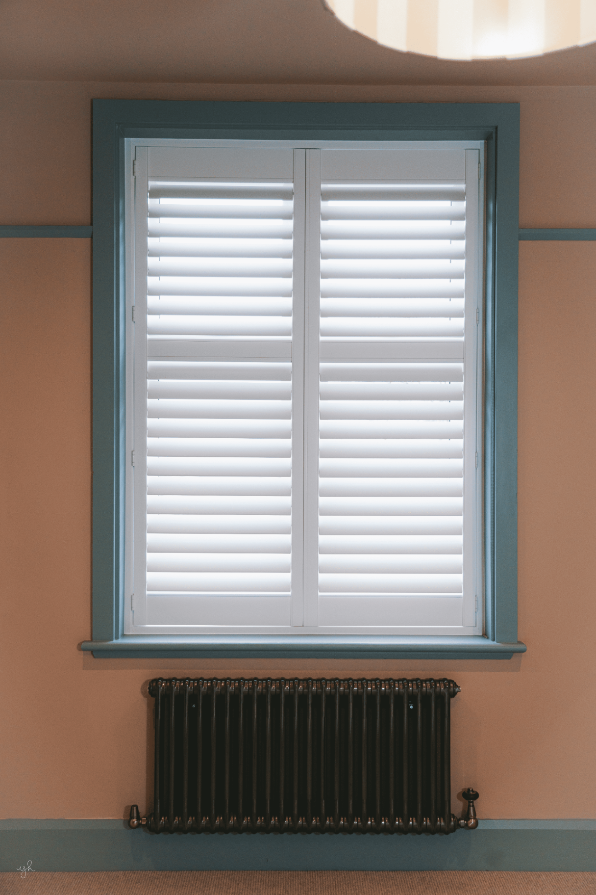 Window shutters with a coloured frame and cast iron radiator below