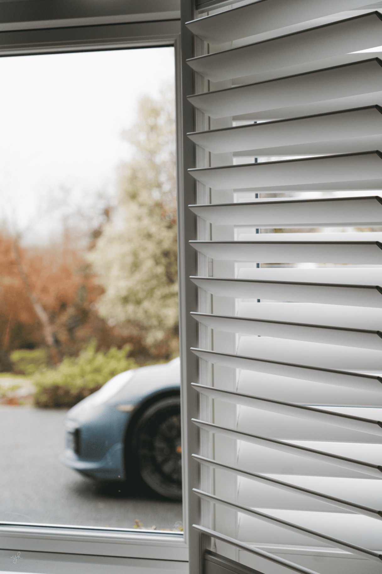 Close-up louvre detail of white shutters with a Porsche visible outside